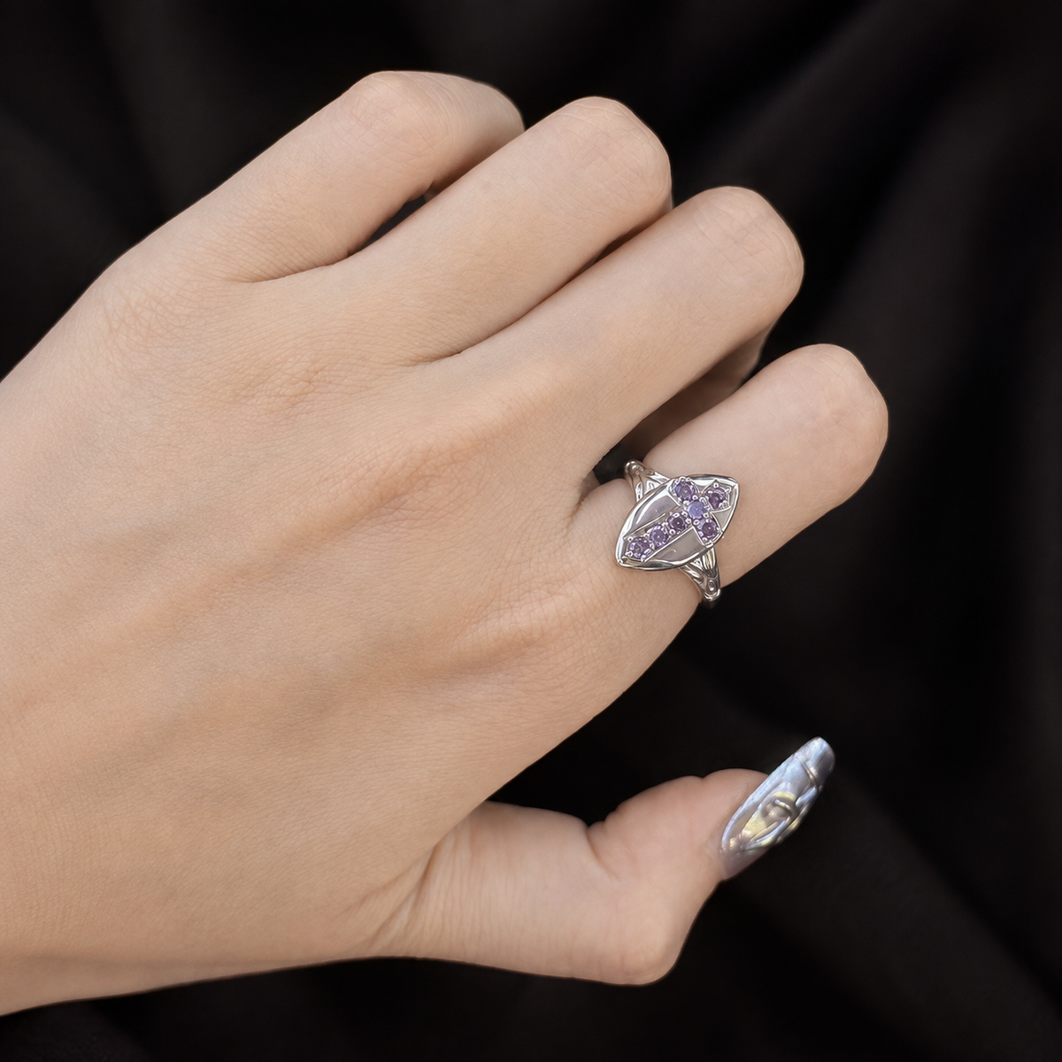 Adjustable gothic purple cross ring worn on a hand against a dark fabric background